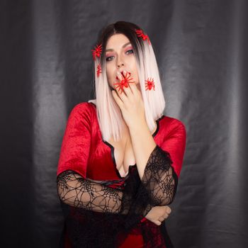 Young beautiful blonde woman in a red vampire dress on a black background. She has a lot of red little spiders