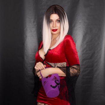 Young beautiful blonde woman in a red vampire dress holds a Halloween purple bag with bats for sweets