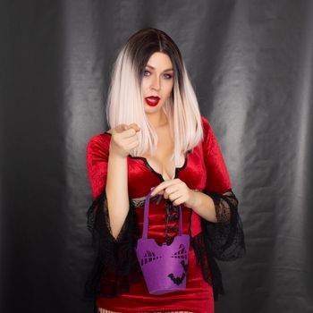 Young beautiful blonde woman in a red vampire dress holds a Halloween purple bag with bats for sweets