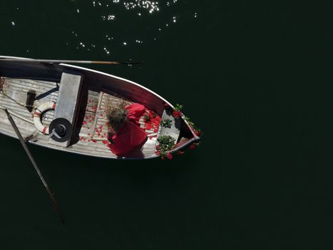 woman with long blond hair on boat with roses and flowers on blue lake