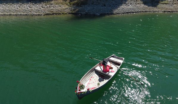 woman with long blond hair on boat with roses and flowers on blue lake