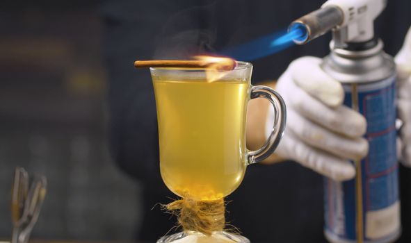 Pouring White Mulled Wine. Close up bartender's hand setting fire on cinnamon stick