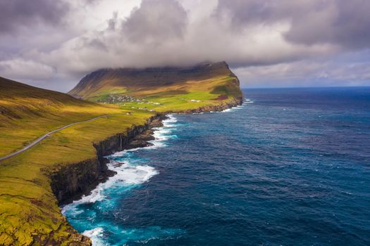 Aerial view of a road going along the atlantic coast to the village of Vidareidi on Faroe Islands surrounded by beatiful scenery.