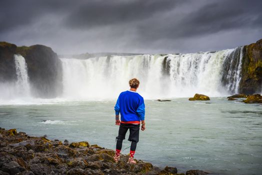 Young hiker standing at the Godafoss waterfall in Iceland. Godafoss means the waterfall of the gods in icelandic.