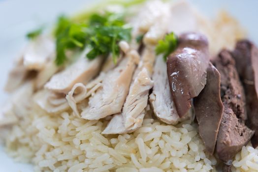 Rice steamed with chicken soup (hainanese chicken rice) with cucumber, liver and sauce for sale at Thai street food market or restaurant in Bangkok Thailand