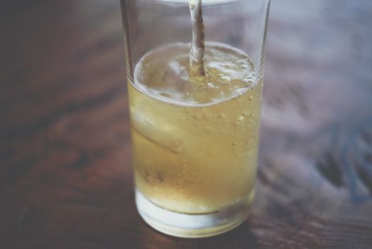 Pouring brewing cold beer water in to beer glass with ice and froth in brewery pub or restaurant on a wood table