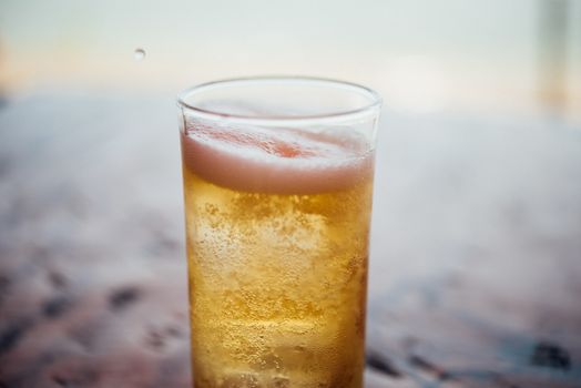 Fresh cold beer water in to beer glass with ice and froth in brewery pub or restaurant on a wood table