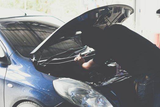 Car mechanic or serviceman checking a car engine for fix and repair problem at car garage or repair shop