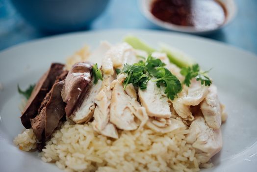 Rice steamed with chicken soup (hainanese chicken rice) with cucumber, liver and sauce for sale at Thai street food market or restaurant in Bangkok Thailand