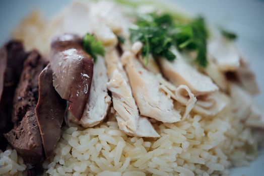 Rice steamed with chicken soup (hainanese chicken rice) with cucumber, liver and sauce for sale at Thai street food market or restaurant in Bangkok Thailand