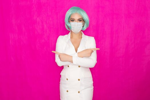 Beautiful young woman with short blue hair in a white business dress jacket with a medical mask posing on a pink background in the studio