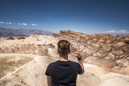 Happy visitor standing on the rim of Zabriskie point in Death Valley National Park in California and doing okay gesture with his hand.