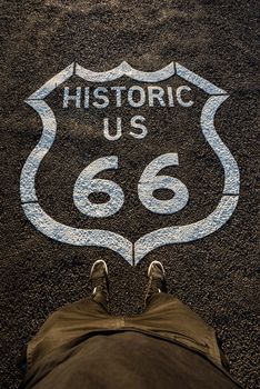 Historic route 66 mark on asphalt surface and a person standing next to it. High detail image.