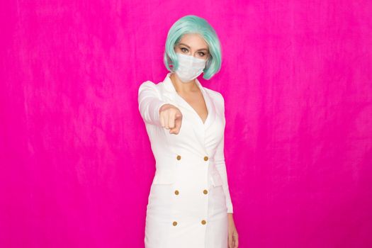 Beautiful young woman with short blue hair in a white business dress jacket with a medical mask posing on a pink background in the studio