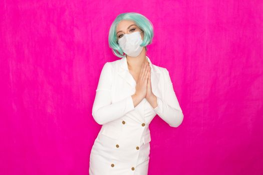 Beautiful young woman with short blue hair in a white business dress jacket with a medical mask posing on a pink background in the studio