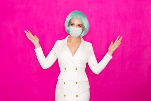 Beautiful young woman with short blue hair in a white business dress jacket with a medical mask posing on a pink background in the studio