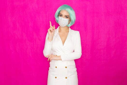 Beautiful young woman with short blue hair in a white business dress jacket with a medical mask posing on a pink background in the studio