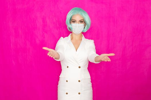 Beautiful young woman with short blue hair in a white business dress jacket with a medical mask posing on a pink background in the studio