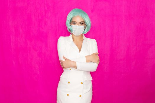 Beautiful young woman with short blue hair in a white business dress jacket with a medical mask posing on a pink background in the studio