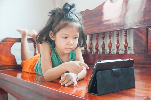 Young Girl lying on wooden stool and Learning online course on Wireless Digital Tablet while staying at home in situation of Corona Virus or Covid 19 outbreak.