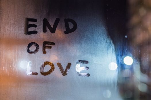 the words end of love handwritten on night wet window glass, closeup with selective focus and bokeh blur