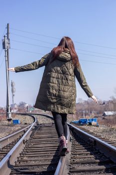 The girl is walking on the railway in front. Rear view