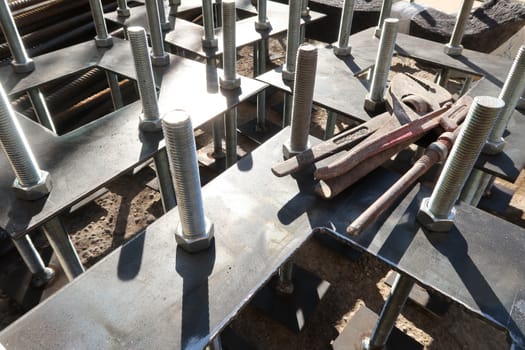 Construction site for a building with a steel structure. Plates with anchor bolts for mounting steel columns on a reinforced concrete foundation. Wrenches supported.