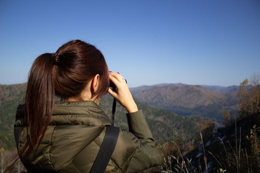 A woman looking at a beautiful landscape, the sea and the mountains through binoculars from the lookout