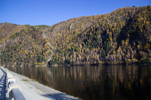 A wide river that lies in the mountain valley. Mountains near the river are covered with forests.