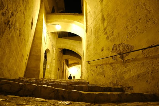 Street with night light in the city of Matera in Italy. Beige tufa stone houses.