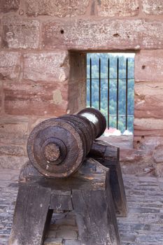 Old black cannon pointing through an opening in a castle rampart with the sea in the background