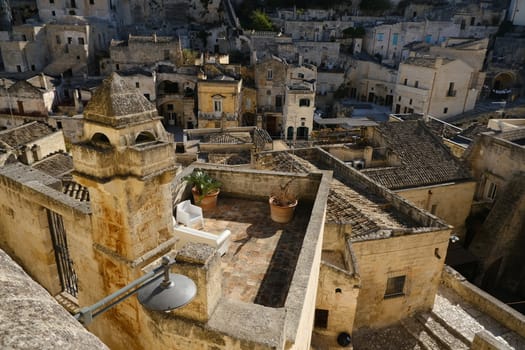 Roofs of houses in the Sassi of Matera transformed into hotels. Panoramic terrace with sofa and chair in white plastic.