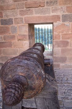 Old black cannon pointing through an opening in a castle rampart with the sea in the background