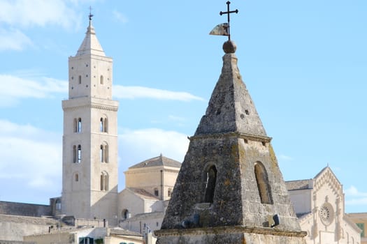 Point of two bell towers and church in the ancient city of Matera in Italy. Construction with blocks of tufa stone. Chileo blue with clouds.