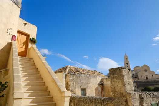 Matera, Basilicata, Italy. About 11/2019. Matera alley with staircase and church. A Mediterranean courtyard with leaves of a small tree blowing in the wind.