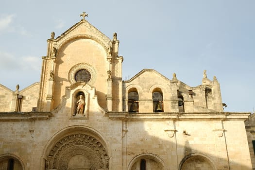 Detail of the church of San Giovanni Battista in Matera. Facade in tufa stone. Bells and statue of the saint and portal in Arabic style.