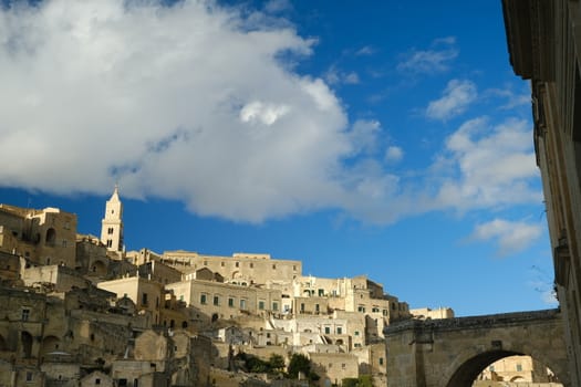 Panorama of the Sassi of Matera with houses in tuff stone. Church with bell tower and stone arch at dawn with sky and clouds.