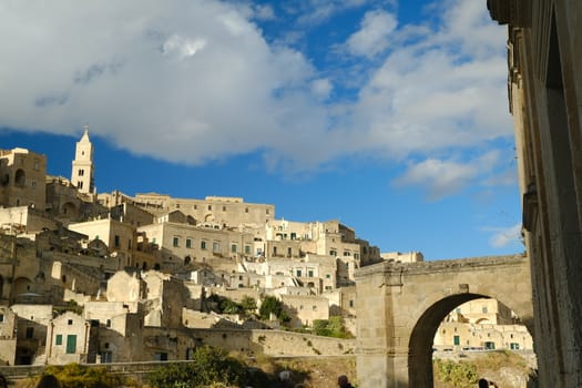 Matera, Basilicata, Italy. About 11/2019.  Panorama of the Sassi of Matera with houses in tuff stone. Church with bell tower and stone arch at dawn with sky and clouds.