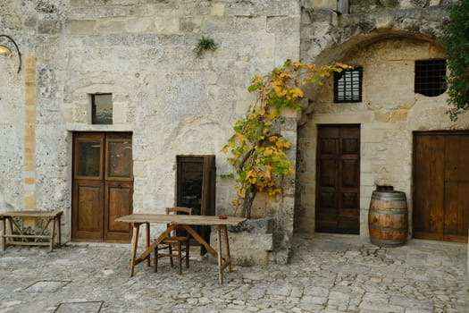 Matera, Basilicata, Italy. About 11/2019. Vine plant grown in a stone planter in the Sassi of Matera. Courtyard of a house with a wooden table and a wine barrel.