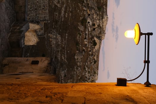 Street lamp lit on a street in Matera. In the background mountain with prehistoric caves used as dwellings.