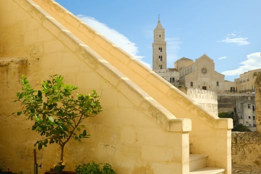 Matera alley with lemon plant and church. A Mediterranean courtyard with leaves of a small tree blowing in the wind.