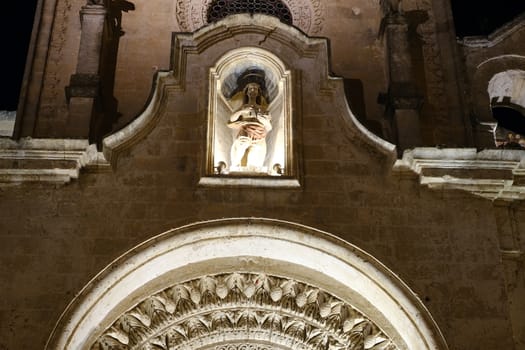 Night photo of the facade of the church of San Giovanni in Matera. Photographed with artificial lights. Detail of the sculpture and the portal in Arabic style.