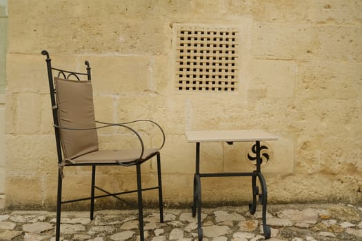 Chair with iron table in a courtyard in the city of Matera. Beige stone wall with marble air grilles.