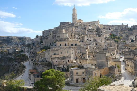 View of the city of Matera in Italy. Church with bell tower and houses built in beige tuff stone.