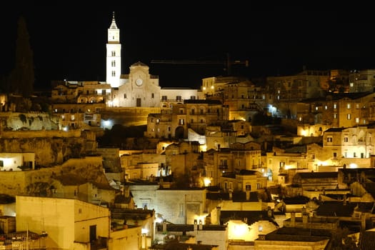 Night panorama of the city of Matera in Italy. Streets, church with bell tower and houses illuminated by artificial yellow lights.