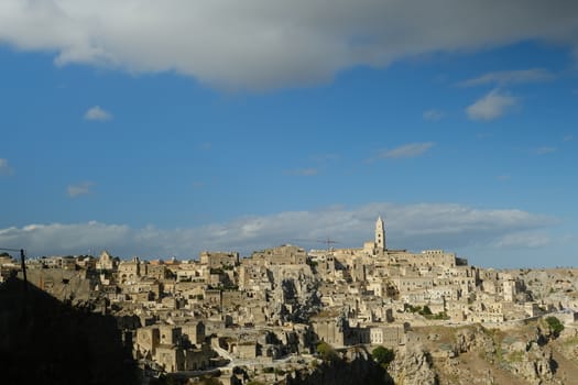 Panorama of houses and of the Sassi of Matera with roofs and streets. Blue sky with church and bell tower with blue sky background with clouds.