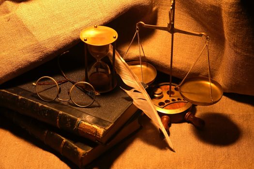 Old books and quill pen near hourglass on canvas background