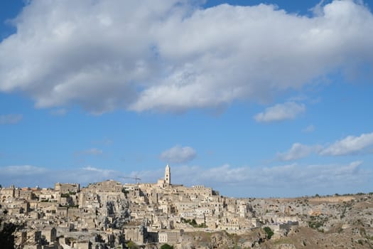 Panorama of houses and of the Sassi of Matera with roofs and streets. Blue sky with church and bell tower with blue sky background with clouds.