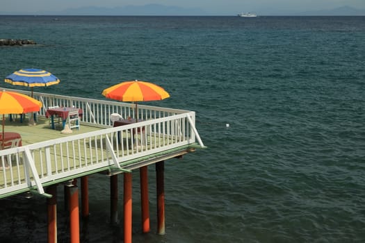 Ischia, Naples, Italy, About the July 2019.  Umbrella on a pier with a white parapet on the sea of Ischia. In the background a ferry boat.