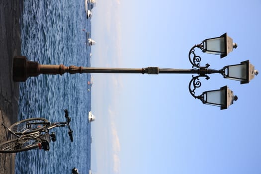 Ischia, Naples, Italy, About the July 2019.  Nineteenth-century street lamp and parked bicycle. In the background the blue sea.